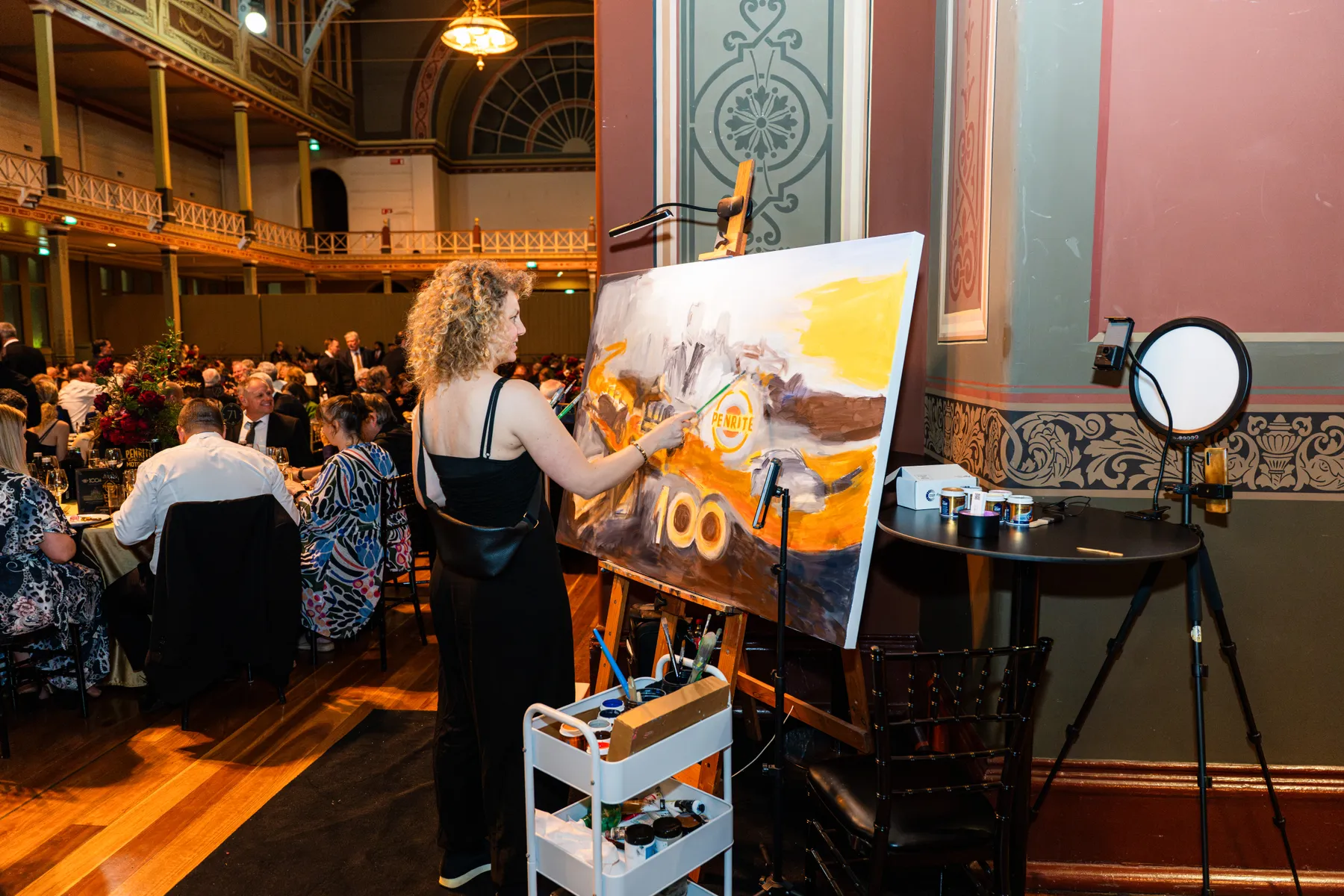 The Penrite painting taking shape beside the seated gala guests